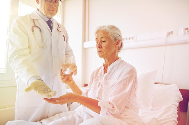 Photo medicine, age, health care and people concept - doctor giving medication and water to senior woman at hospital ward