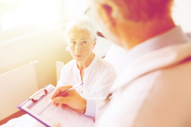 Photo medicine, age, health care and people concept - senior woman and doctor writing to clipboard at hospital ward