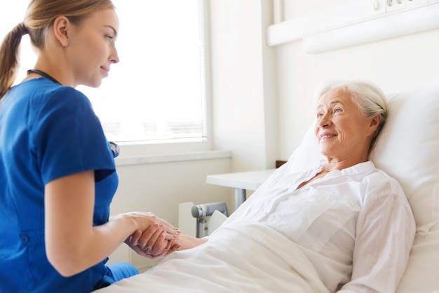 의학, 나이, 지원, 건강 관리 및 사람 개념 - 병원 병동에서 침대에 누워 있는 노인 여성을 방문하고 응원하는 의사 또는 간호사