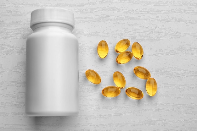 Medicine bottle and cod liver oil capsules on white wooden background