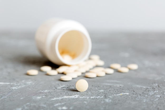 Medicine bottle and white pills spilled on a light background\
medicines and prescription pills flat lay background white medical\
pills and tablets spilling out of a drug bottle