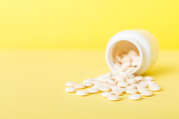 Medicine bottle and white pills spilled on a light background Medicines and prescription pills flat lay background White medical pills and tablets spilling out of a drug bottle