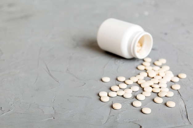 Medicine bottle and white pills spilled on a light background Medicines and prescription pills flat lay background White medical pills and tablets spilling out of a drug bottle