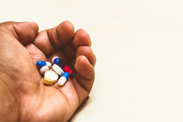 Medicine capsules (assorted pills) in a man's hand. Light background. Concept of self-medication, health, depression, cancer, medications.