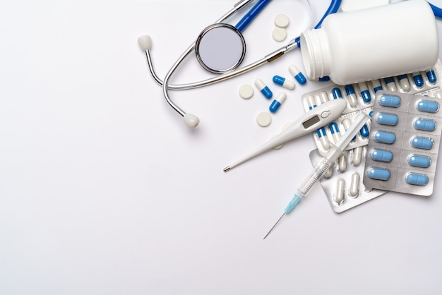 Medicine concept - pills, syringe, thermometer and stethoscope onlight grey background with copy space