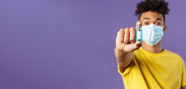 Medicine coronavirus and people concept closeup portrait of young man in facial mask holding ampoule...