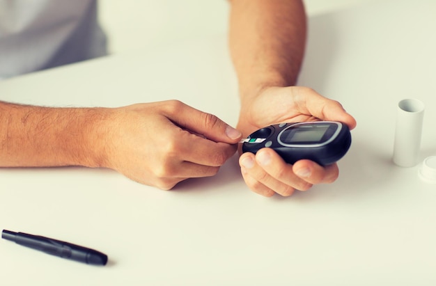 Photo medicine, diabetes, glycemia, health care and people concept - close up of man checking blood sugar level by glucometer at home