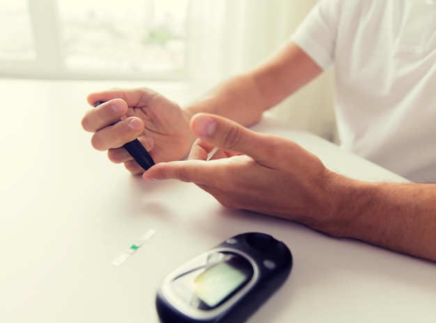 medicine, diabetes, glycemia, health care and people concept - close up of man checking blood sugar level by glucometer at home