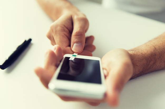 Photo medicine, diabetes, glycemia, health care and people concept - close up of man with smartphone checking blood sugar level by glucometer at home