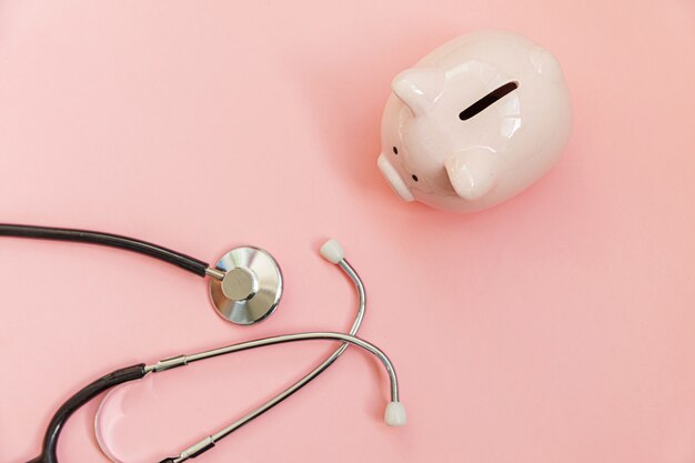 Photo medicine doctor equipment stethoscope and piggy bank isolated on pink pastel background. health care financial checkup or saving for medical insurance costs concept.