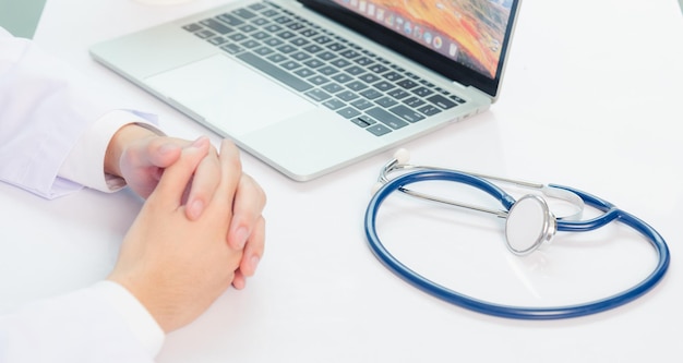 Foto il medico di medicina sta lavorando alla scrivania. primo piano dello stetoscopio. la videochiamata dell'uomo medico si siede mano nella mano e ascolta la spiegazione del paziente sul computer portatile anteriore presso l'ufficio dell'ospedale, concetto medico sanitario