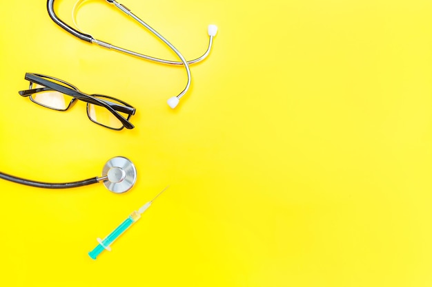 Medicine equipment stethoscope or phonendoscope glasses and syringe isolated on trendy yellow backgr...