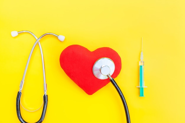 Medicine equipment stethoscope syringe and red heart isolated on yellow background