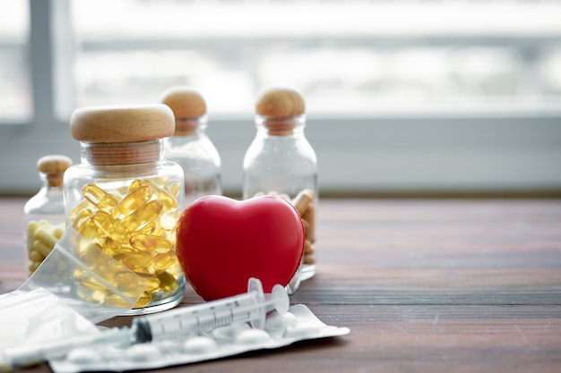 Medicine in glass bottle and heart on wood table.