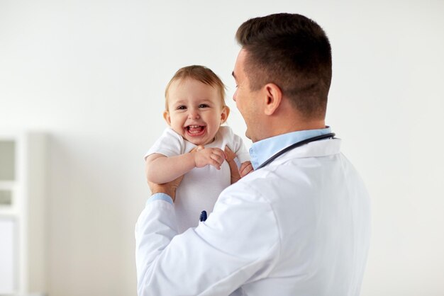 의학, 의료, 소아과 및 사람 개념 - 행복한 의사 또는 소아과 의사가 클리닉에서 의료 검사에서 아기를 들고 있습니다.