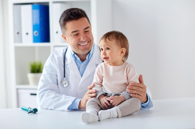 Photo medicine, healtcare, pediatry and people concept - happy doctor or pediatrician holding baby on medical exam at clinic