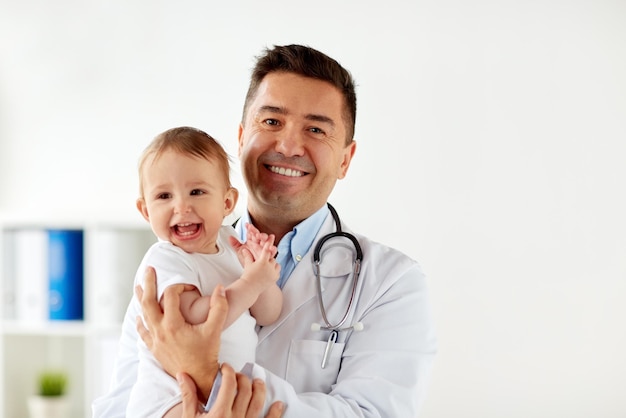 medicine, healtcare, pediatry and people concept - happy doctor or pediatrician holding baby on medical exam at clinic