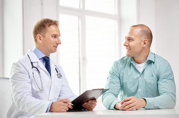 medicine, health care, people and prostate cancer concept - happy male doctor with clipboard and patient meeting and talking at hospital