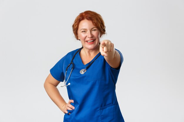 Medicine, healthcare   concept. Cheerful smiling and enthusiastic middle-aged doctor, female redhead nurse pointing finger at camera