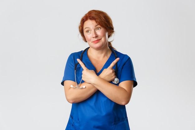 Medicine, healthcare   concept. Indecisive dreamy middle-aged redhead doctor, female nurse making choice, pointing fingers sideways