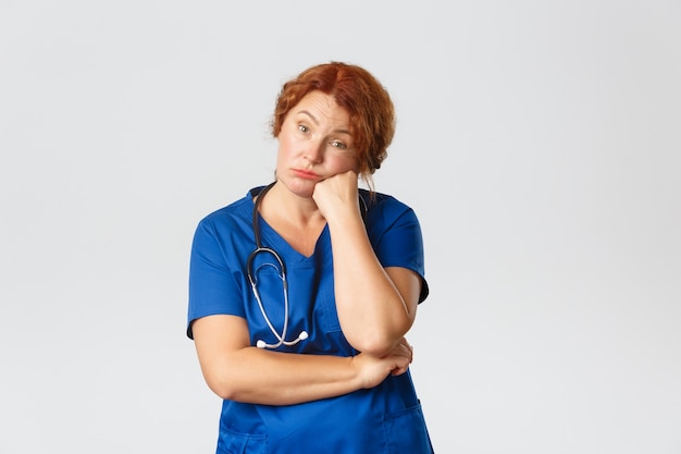 Medicine, healthcare and coronavirus concept. Bored and tired middle-aged female retirement home nurse, medical worker at clinic or doctor in scrubs looking unamused, sitting on boring meeting.