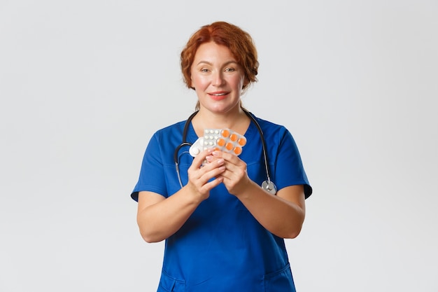 Medicine, healthcare and coronavirus concept. Smiling redhead female doctor, physician prescribe medication, treatment from flu, influenza or allergy, showing tablets, recommend pills.