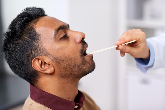 Photo medicine healthcare and laryngology concept doctor or laryngologist hand with tongue depressor examining male patient throat at clinic