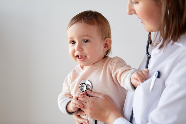 Photo medicine, healthcare, pediatry and people concept - close up of doctor with stethoscope listening to baby on medical exam at clinic