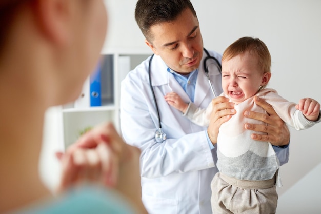Photo medicine, healthcare, pediatry and people concept - doctor or pediatrician holding sad crying baby girl on medical exam at clinic