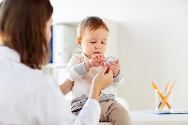 Photo medicine, healthcare, pediatry and people concept - doctor with stethoscope listening to happy smiling baby girl on medical exam at clinic