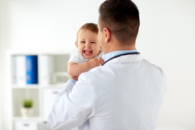 medicine, healthcare, pediatry and people concept - happy doctor or pediatrician holding baby on medical exam at clinic