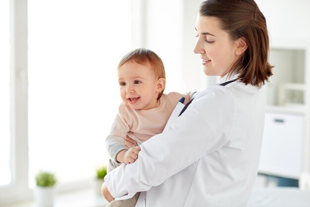 medicine, healthcare, pediatry and people concept - happy doctor or pediatrician holding baby on medical exam at clinic