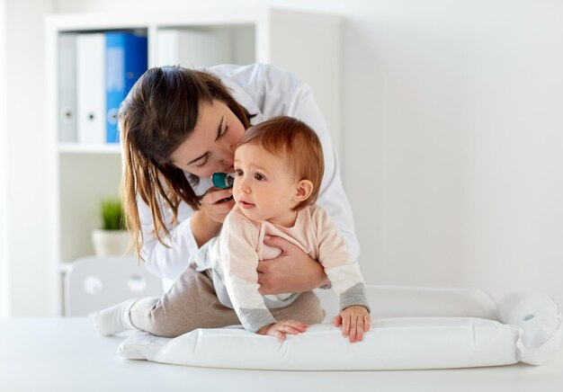 Photo medicine, healthcare, pediatry and people concept - otolaryngologist or doctor checking baby ear with otoscope and young woman at clinic