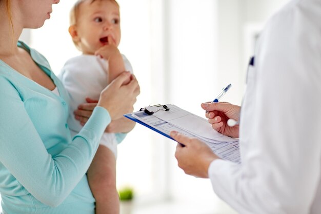 Photo medicine, healthcare, pediatry and people concept - woman with baby and pediatrician or doctor with clipboard at clinic