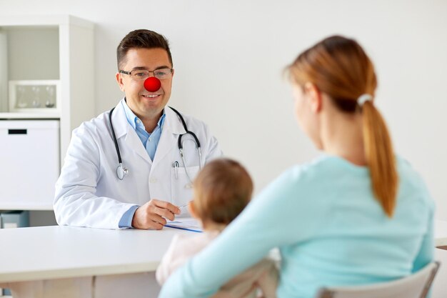 medicine healthcare pediatry and red nose day concept happy woman with baby and doctor at clinic