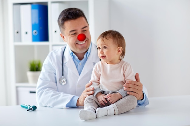 Photo medicine healthcare pediatry and red nose day concept sweet baby girl and doctor or pediatrician on medical exam at clinic