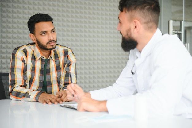 Medicine healthcare and people concept happy doctor with clipboard and young male patient meeting at hospital