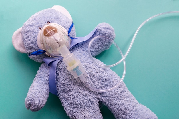 Medicine layout or flat lay. Children's toy masked by inhaler. The blue bear symbolizes the child and childhood.