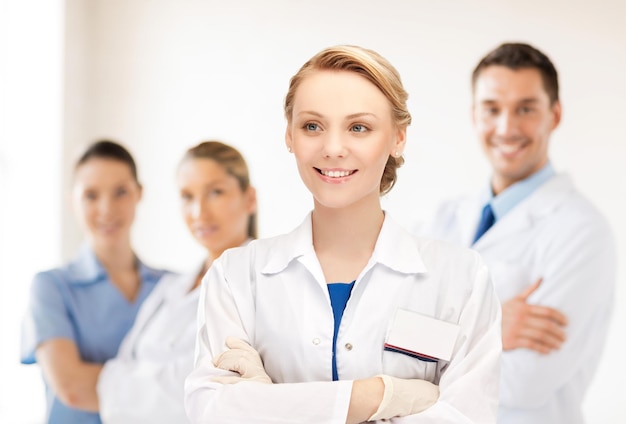 medicine, people, profession and teamwork concept - smiling young female doctor in white coat over group of medics in hospital