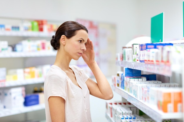 Medicine pharmaceutics healthcare and people concept female customer having headache choosing drugs at pharmacy