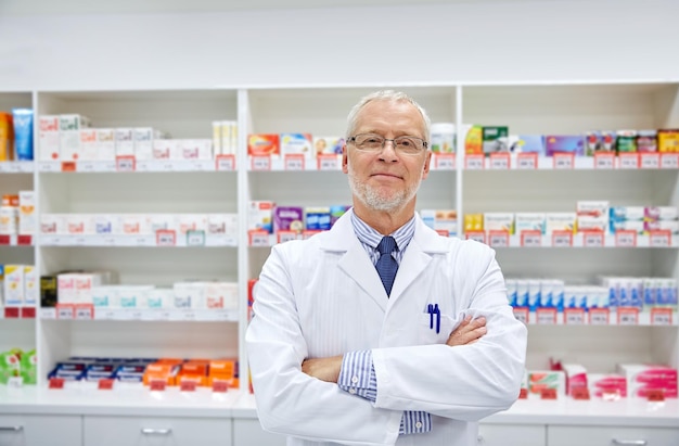 医学、薬局、人、医療、薬学のコンセプト – ドラッグストアで白衣を着た笑顔の上級男性薬剤師