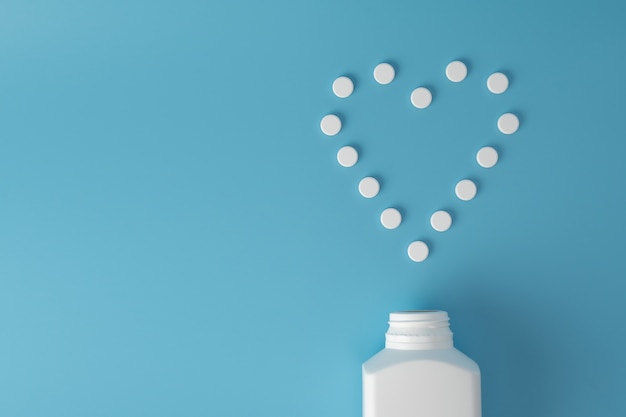 Medicine pills in heart shape on blue surface