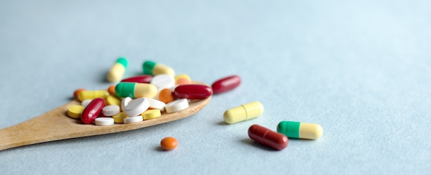 Medicine pills, tablets and capsules in a wooden spoon on a blue table