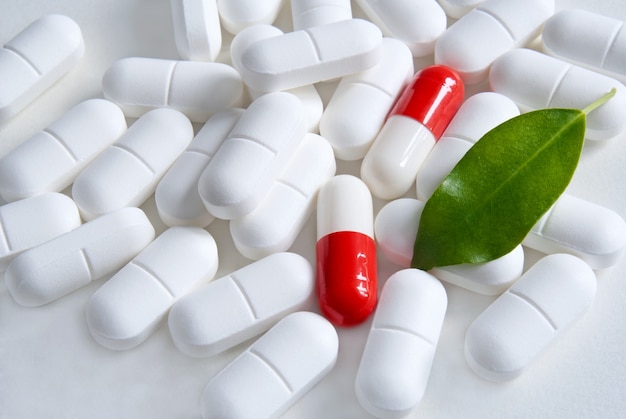 Medicine pills with dry natural herbs on white background