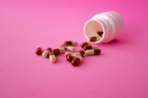 약 분홍색 알약 캡슐과 텍스트를 위한 공간이 있는 분홍색 배경에 분홍색 꽃을 흐리게 합니다. 치유를 위한 약이나 건강한 개념을 위한 비타민. 선택적 초점. 평면도