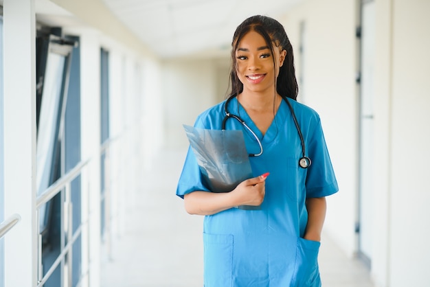Фото Концепция медицины, профессии и здравоохранения - счастливая улыбающаяся афро-американская женщина-врач со стетоскопом на фоне больницы