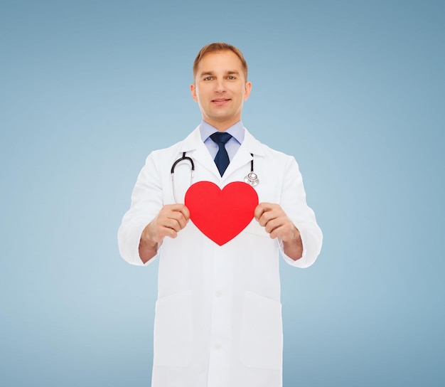 medicine, profession, charity and healthcare concept - smiling male doctor with red heart and stethoscope over blue background