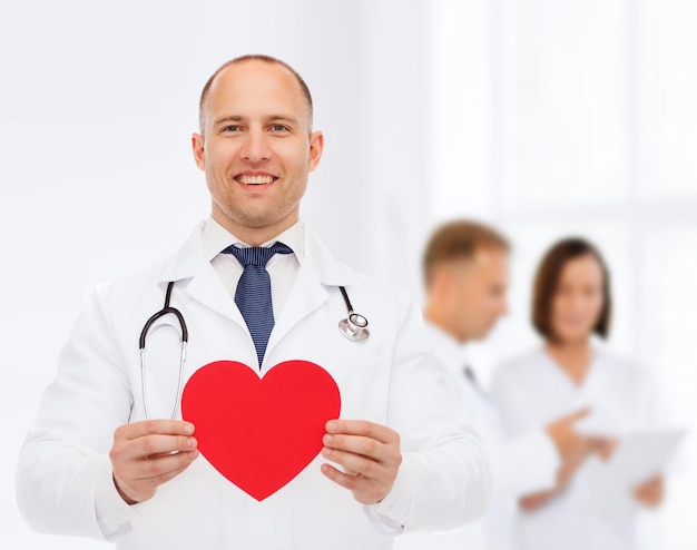 медицина, профессия, благотворительность и концепция здравоохранения - улыбающийся врач-мужчина с красным сердцем и стетоскопом над группой медиков