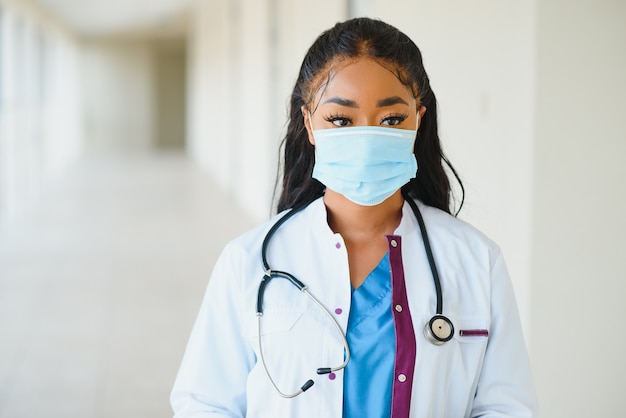 Medicine, profession and healthcare concept - african american female doctor or scientist in protective facial mask in clinic