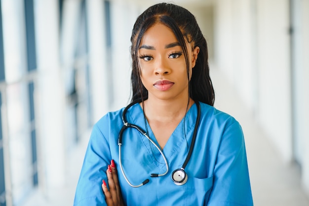 Medicine, profession and healthcare concept - happy smiling african american female doctor with stethoscope over hospital background